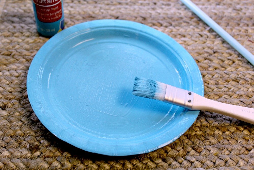 Paper plate painted blue with paintbrush.
